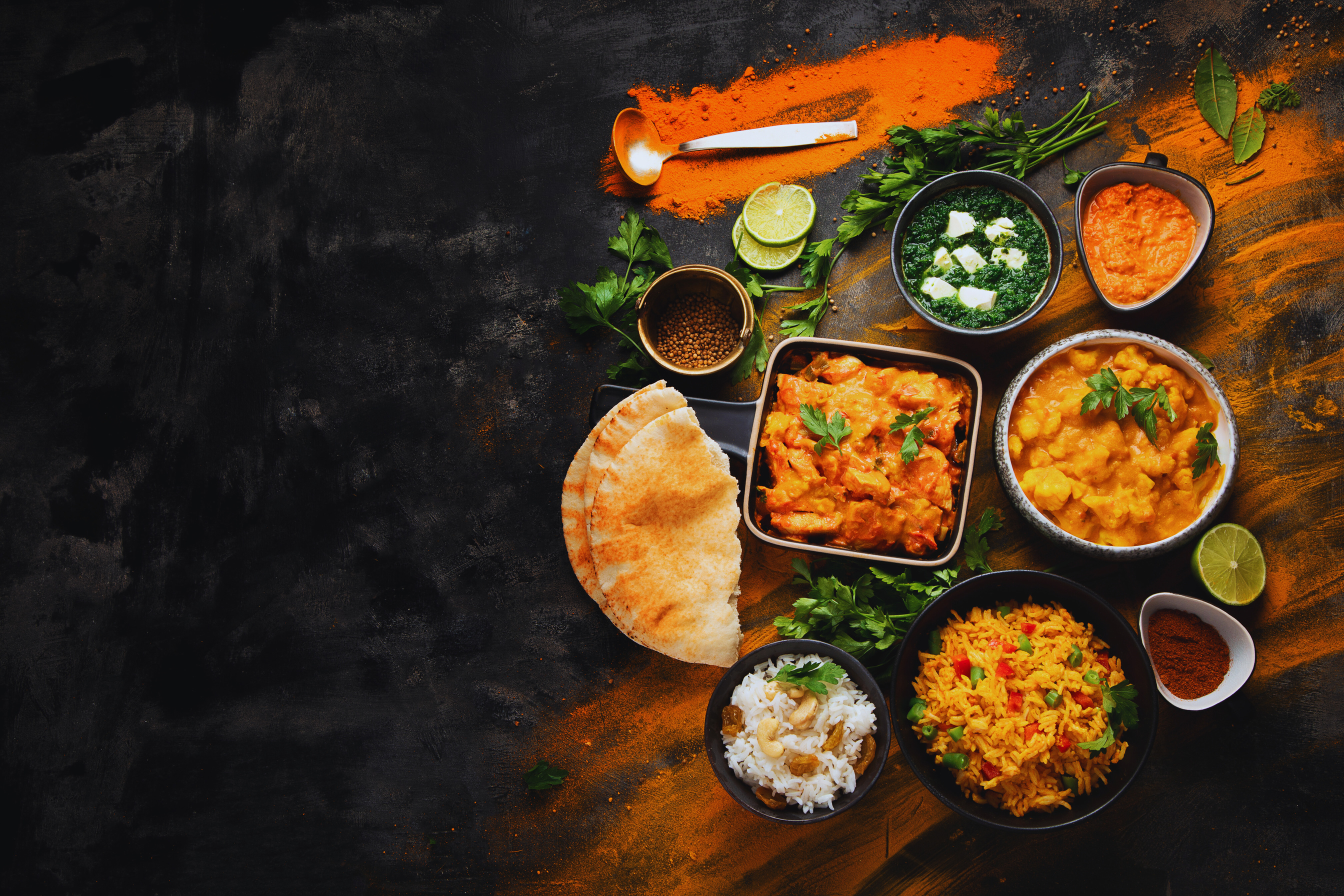 An overhead spread of Indian curries, rice, paratha and fresh herbs
